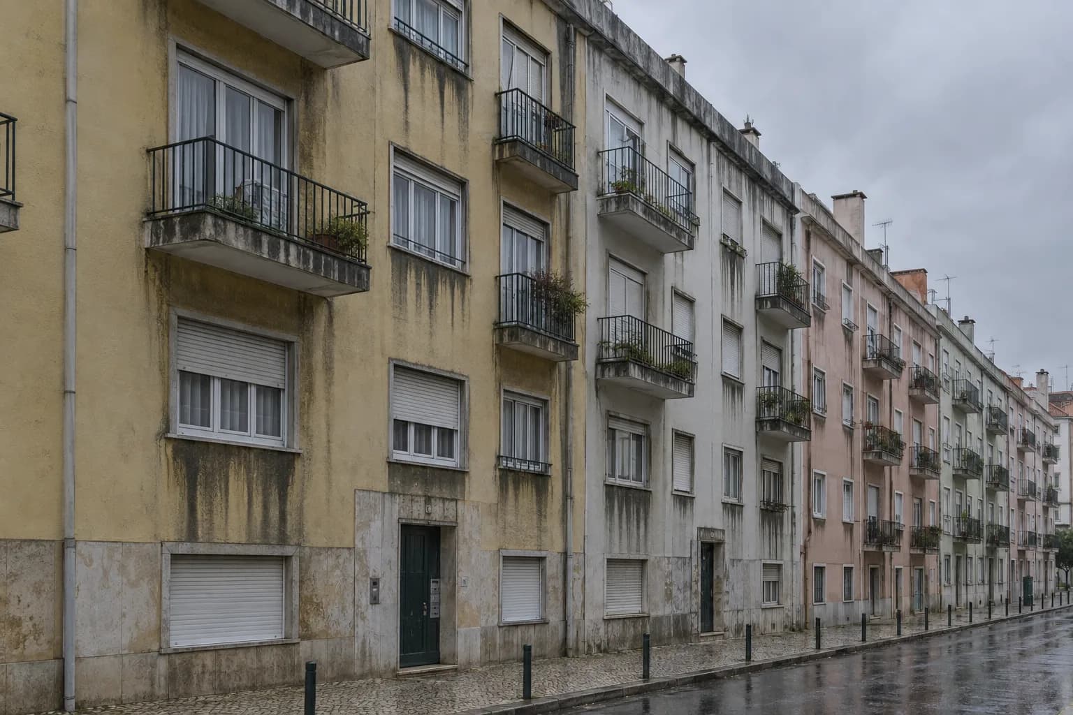 Rua de prédios antigos em dia de chuva, com manchas de humidade a escorrer das varandas e das janelas